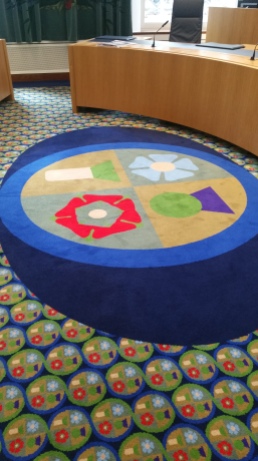 In that carpet there are 4 symbols, each representing the 4 nations of the UK. England- the english rose, Scotland -a purple thistle, Ireland - a blue flax flower and Wales - the green leaves of leeks. They all have a meaning associated it with it. If you can tell me what they mean, i will buy you a beer. :-)